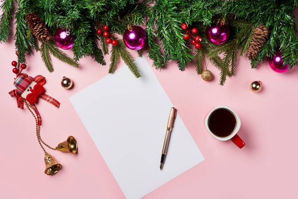 Fondo navideño con peper rodeado de decoraciones navideñas y una taza de café sobre fondo rosa. Carta a Santa o lista de compras de Navidad - Foto, imagen