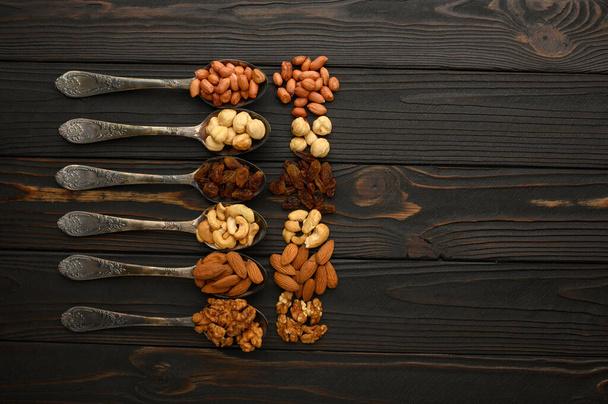 Hazelnut, cashews, raisins, almonds, peanuts, walnuts in silver spoons on a rustic background - Photo, image