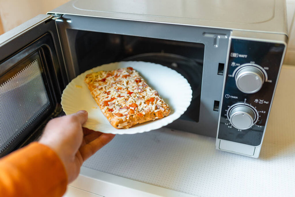 Piccola pizza surgelata cruda inserita nel cibo spazzatura microwave.junk, concetto di fast food Vista laterale.Focus selettivo. - Foto, immagini