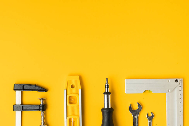 Handyman's tools. Flat lay of clamps, wrench, screwdriver, drill, angle, bubble level and tape measure on yellow background. Happy Father's Day. Free space  for you text - Valokuva, kuva