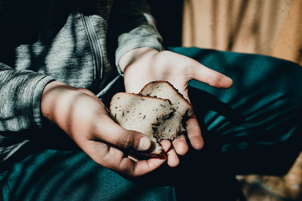 Φτωχό παιδί άστεγο, ζητιανάκι κρατάει ένα κομμάτι μαύρο ψωμί, πολεμική αντίληψη, φτώχεια, κρίση. Επιλεκτική εστίαση.Κοντινό πλάνο.. - Φωτογραφία, εικόνα