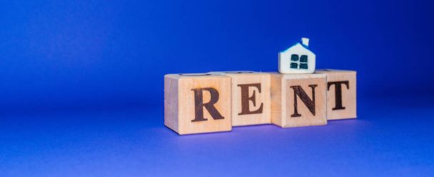 Дерев'яні кубики зі словом RENT з мініатюрним іграшковим будинком на фіолетовому, вечірньому фоні.
. - Фото, зображення