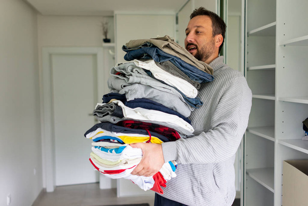 Man tiding outfit from large wardrobe closet with stylish clothes and home stuff. High quality photo - Fotografie, Obrázek