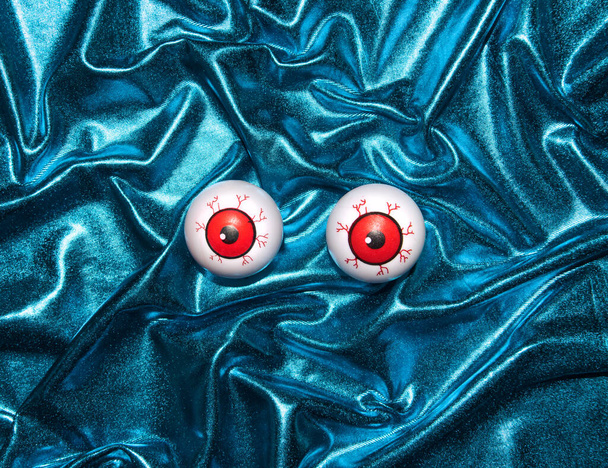 Metalik mavi renkli, yaratıcı kumaş arkaplanda komik göz küreleri. Asgari korku düzeni. - Fotoğraf, Görsel