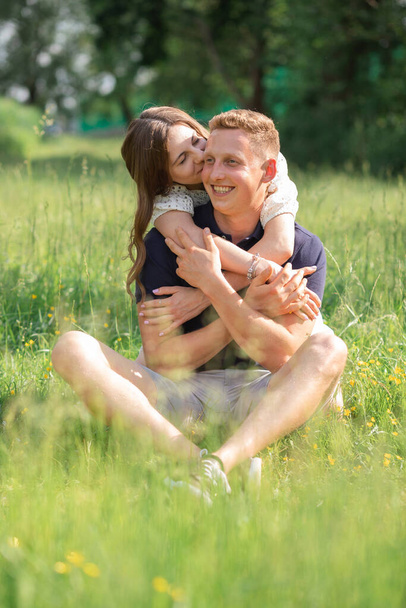 Joli jeune couple assis sur l'herbe dans le parc, embrasser. Jeune homme et jeune femme profitant de la journée d'été. Heureux les amoureux, lune de miel - Photo, image