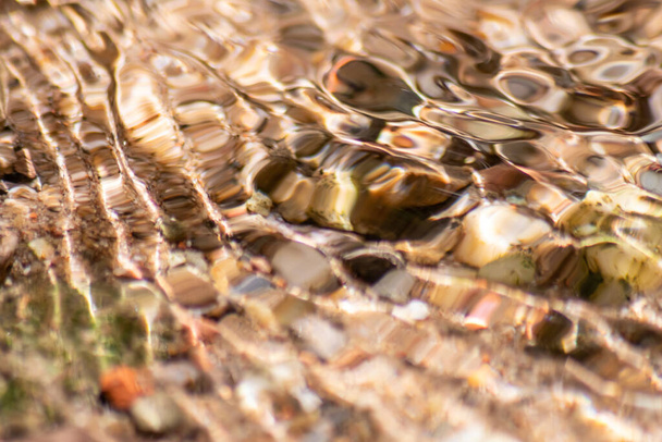 Steine im glitzernden Wasser mit sonnigen Reflexen im Wasser eines kristallklaren Wasserbaches als idyllischer natürlicher Hintergrund zeigen Zen-Meditation, kleine Wellen und seidige Wellen in einer gesunden Bergquelle - Foto, Bild