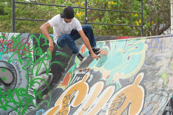 Młody deskorolkarz skaczący na rampie. Młody człowiek na deskorolce z pomalowaną graffiti ścianą. - Zdjęcie, obraz