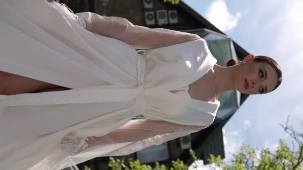 Hermoso clip vertical. Una mujer hermosa camina a través de un puente en ropa interior hermosa y una túnica blanca. La cámara se mueve con el modelo. Slo-mo. - Metraje, vídeo