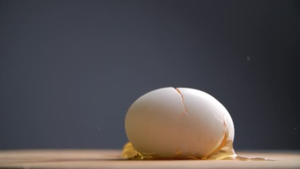 Zeitlupe eines frischen Eies, das gegen einen Holztisch kracht. Nahaufnahme einer zubereiteten Speise. Hochwertiges FullHD-Filmmaterial - Filmmaterial, Video