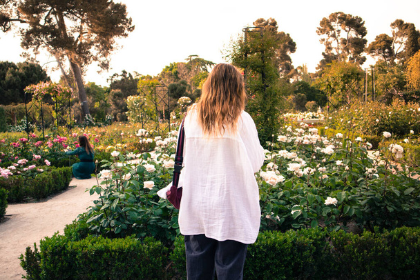 Madrid, Spanyolország. 2022. június 1. Emberek a rozáriumban. Fiatal nő sétál a városi parkban, botanikus rózsakert nyáron. Sok cserje virágzó fehér virágokkal. Arctalan trend. Ember és természet. - Fotó, kép