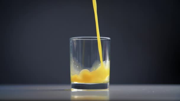 Close-up de um suco de laranja fresco derramando em um copo. Movimento lento de uma bebida de cor viva derramada em uma xícara. Imagens FullHD de alta qualidade - Filmagem, Vídeo