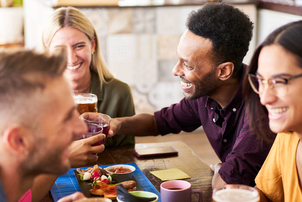 Ryhmä hauskoja ihmisiä juo olutta baarissa. 30s Nuoret ystävät hauskaa ja lounasta ja alkoholia katolla happy hour. Laadukas kuva - Valokuva, kuva