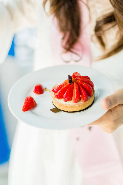 Un primer plano de una mano de mujer sosteniendo un pastel dulce con fresas - Foto, Imagen