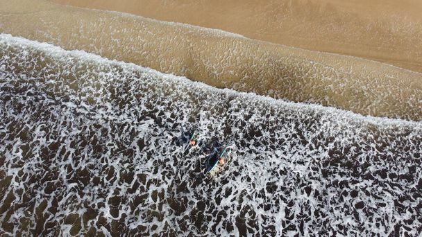 Αεροφωτογραφία δύο ανθρώπων να κρατούν σανίδες στη θάλασσα έτοιμες να σερφάρουν. - Φωτογραφία, εικόνα