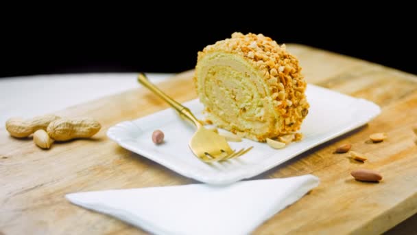 Gâteau aux cacahuètes sur une assiette avec une fourchette en or. En arrière-plan se trouvent des cacahuètes pelées sur un plateau de cuisson de style rétro. Macro et curseur de tir. - Séquence, vidéo