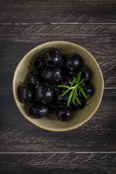 Olives in a ceramic bowl on a wooden table. - Foto, Bild