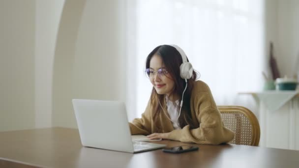 Young asian woman wearing glasses and headset working on computer laptop at house. Work at home, Video conference, Video call, Student learning online class - Metraje, vídeo