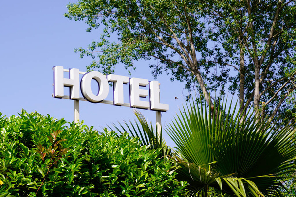 Mavi gökyüzünde yeşil palmiye ağaçlı otel tabelası. - Fotoğraf, Görsel