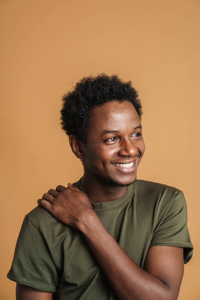 Young black man wearing t-shirt smiling and looking aside isolated over beige background - Foto, Bild