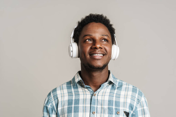 Μαύρος άνδρας χαμογελά ακούγοντας μουσική με ακουστικά απομονωμένα σε λευκό φόντο - Φωτογραφία, εικόνα