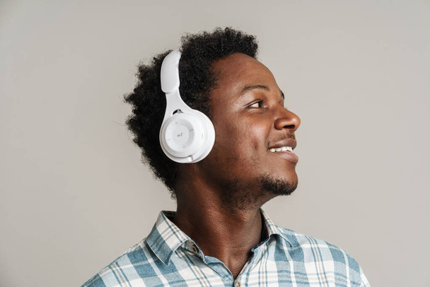 Young black man smiling while listening music with headphone isolated over white background - Foto, Imagen