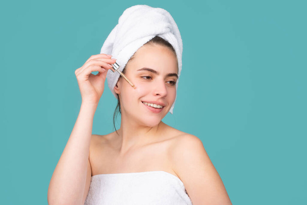 Beautiful woman moisturizing face with oil. Beauty face of a cheerful attractive girl with towel on head, isolated. Moisturized healthy skin, morning spa, beauty routine, facial skincare treatment - Photo, Image