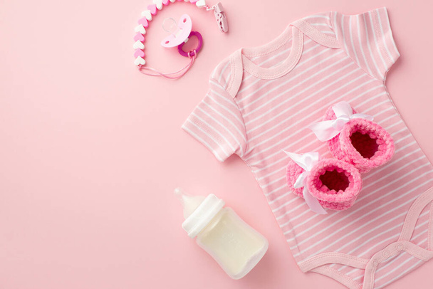 Baby accessories concept. Top view photo of pink bodysuit knitted booties pacifier chain and bottle on isolated pastel pink background - Foto, Imagem