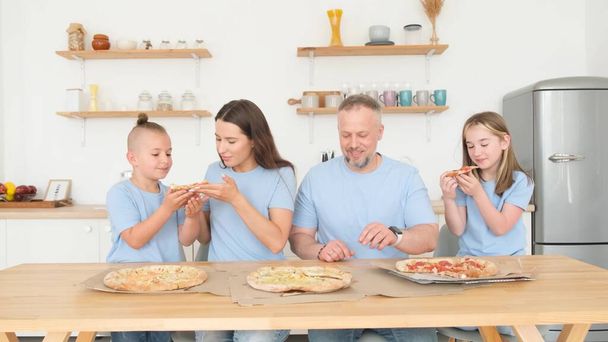 Die amerikanische Familie isst zu Hause Pizza, sie sitzen am Tisch in der Küche. Glückliche junge Familie beim Abendessen - Foto, Bild