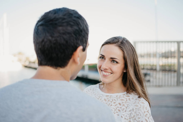 彼のブルネットのガールフレンドが夜にスペインの桟橋の近くを見つめているスタイリッシュな男の後ろからの写真。バレンシアでの日付の観光客のカップル - 写真・画像