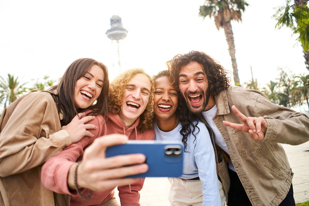Çok ırklı bir grup insan telefonla gülümseyen bir selfie çekiyor. Mobil fotoğraf çeken neşeli arkadaşlar birlikte eğleniyorlar. Yüksek kalite fotoğraf - Fotoğraf, Görsel