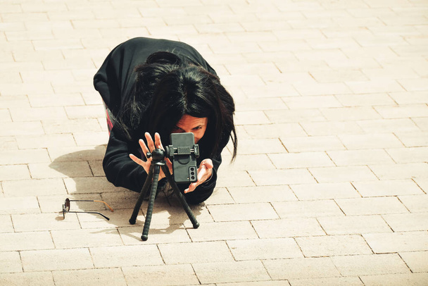 Захоплена молода брюнетка біла жінка подорожує фотограф стріляти зі смартфона на тринозі на відкритому повітрі в громадських місцях в туристичному напрямку
 - Фото, зображення