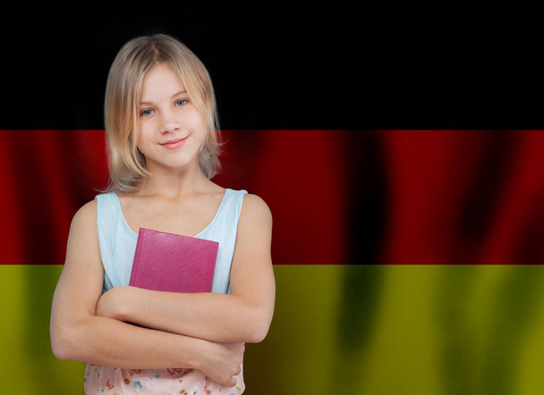 Χαμογελαστή νεαρή κοπέλα με βιβλίο με φόντο τη γερμανική σημαία. Εκπαίδευση και σχολείο στη Γερμανία.  - Φωτογραφία, εικόνα