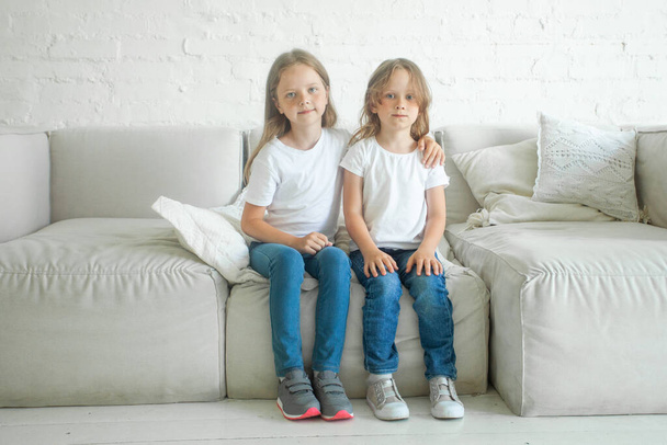 Two little girls sisters hugging and sitting on sofa indoor - Photo, Image