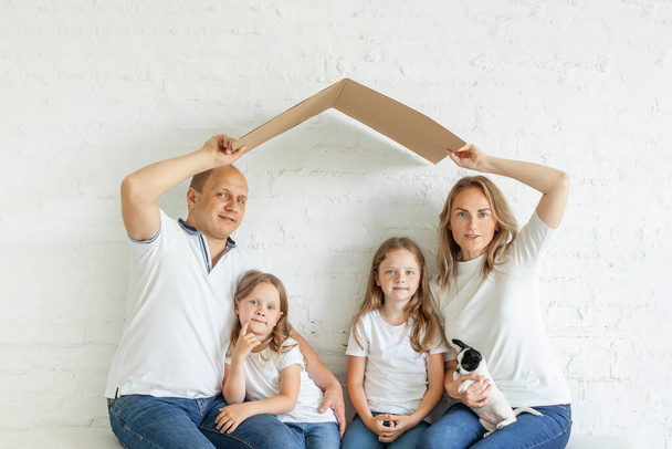 Onnellinen perhe, jolla on kaksi lasta sisätiloissa valkoista seinää vasten. Vakuutus, muuttopäiväkoti, omaisuus ja sijoituskäsite - Valokuva, kuva