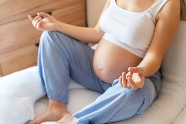 Meditación saludable durante el embarazo. Mujer embarazada hermosa meditando mientras está sentada en posición de loto. Salud yoga deporte en casa. Embarazo, maternidad, concepto de salud - Foto, Imagen