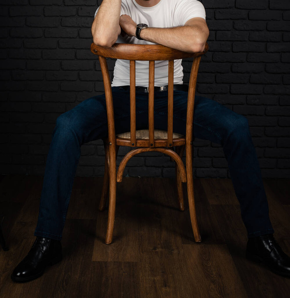 An unrecognizable man in a white T-shirt with a watch on his arm sits on a chair. - Fotografie, Obrázek
