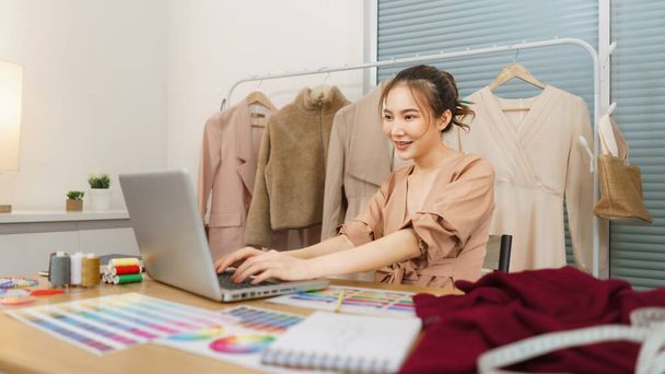Σχεδιασμός μόδας έννοια, ασιατική γυναίκα σχεδιαστής χρησιμοποιούν φορητό υπολογιστή για την αναζήτηση δεδομένων για τη νέα συλλογή. - Φωτογραφία, εικόνα