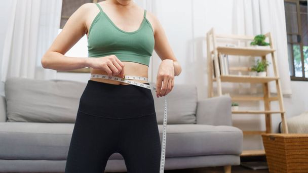 Healthy and weight loss concept, Young Asian woman is measuring her waist with tape measure. - Фото, изображение