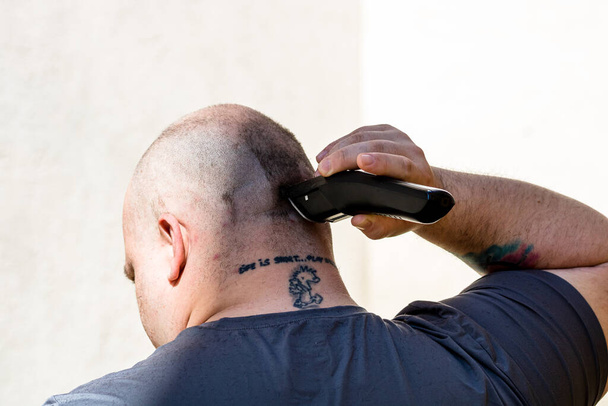 Mężczyzna golący lub strzyżący włosy za pomocą maszynki do strzyżenia lub maszynki do golenia elektrycznego - Zdjęcie, obraz