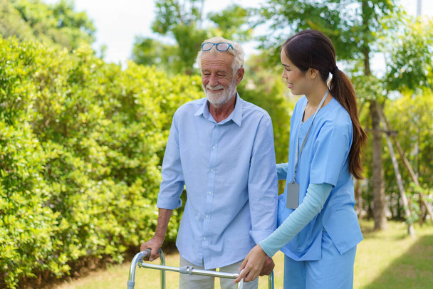 Mujer asiática joven enfermera cuidadora ayudar anciano mayor con caminante movilidad en el jardín en casa. Guardería para adultos mayores, Enfermera cuida a paciente anciano con alegre concentrado - Foto, imagen