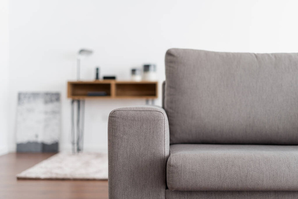 Nahaufnahme der grauen Couch in einer modernen Wohnung vor verschwommenem Hintergrund. Bequemes Sofa im möblierten Wohnzimmer. Konzept für Wohnkultur und neue Haushaltsmöbel - Foto, Bild