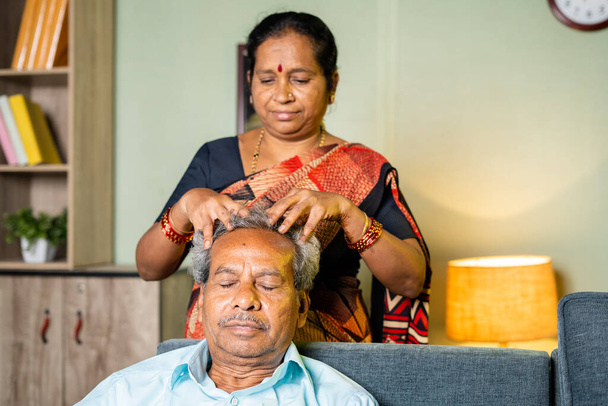 vrouw masseren hoofd van ontspannen man thuis terwijl zitten op de bank - concept van familie, senior paar en bonding - Foto, afbeelding