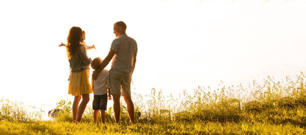 Glücklich liebende Familie, die im Licht des Sonnenuntergangs im Freien spazieren geht. Vater, Mutter, Sohn und Tochter. Hintergrund Meer und Feld - Foto, Bild