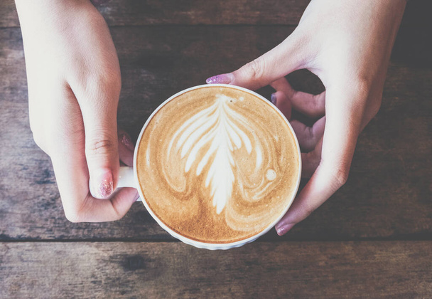 Vista superior de alguém mãos segurando uma xícara de café com leite quente. Café com leite é uma categoria de bebidas à base de café feitas com leite. - Foto, Imagem