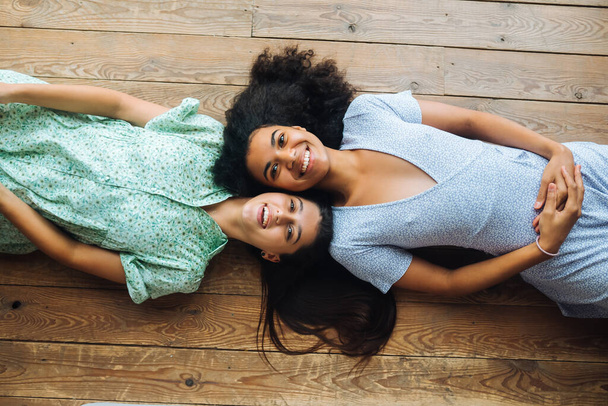 Δύο νεαρές γυναίκες ξαπλώνουν πρόσωπο με πρόσωπο στο πάτωμα, από ψηλά. - Φωτογραφία, εικόνα