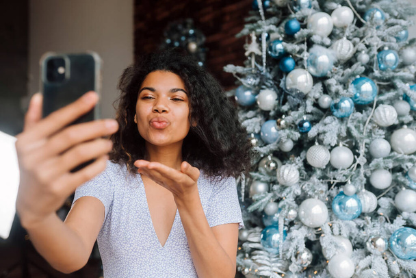 Kaunis nuori hymyilevä nainen lähellä joulukuusi klo Tausta Making Video Message tai Selfie Concept of Holidays ja uusi vuosi joulukoristeluun huoneessa. - Valokuva, kuva