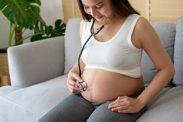 Young pregnant woman putting stethoscope on tummy, healthcare and pregnancy care concept - Foto, Imagem