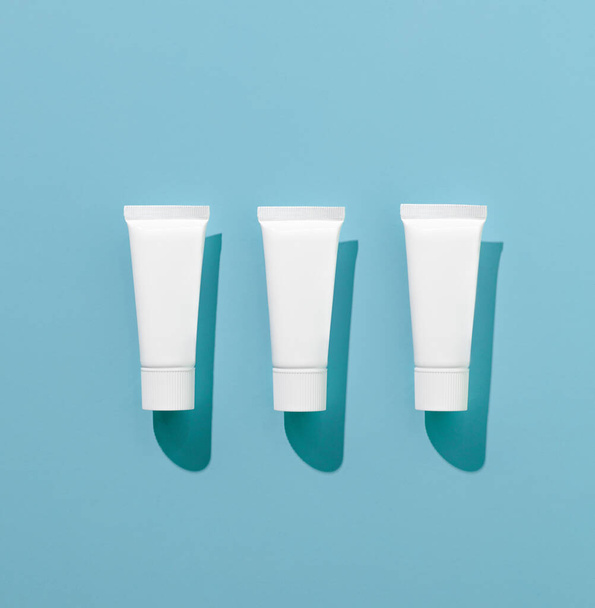 Mockup of clean tubes of toothpaste or cream pattern on blue background with hard shadows. The concept of daily care for teeth and oral cavity. Advertising poster, place for text - Φωτογραφία, εικόνα