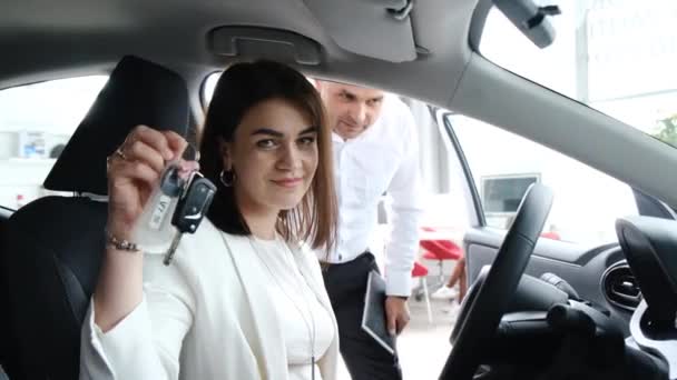 Šťastná brunetka žena ukazující klíč od auta na kameru po koupi nového auta. Koupě nového auta v showroomu - Záběry, video