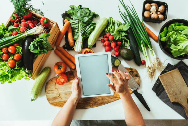 Fermer Photo de mains de femme utilisant une tablette numérique au-dessus d'une table pleine de légumes biologiques - Photo, image